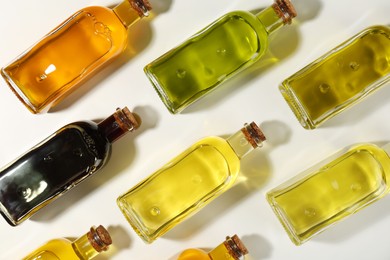 Photo of Vegetable fats. Different cooking oils in glass bottles on white background, flat lay