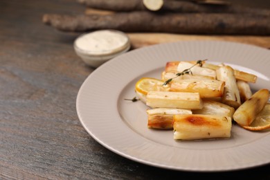 Photo of Plate with baked salsify roots, lemon and thyme on wooden table, closeup. Space for text