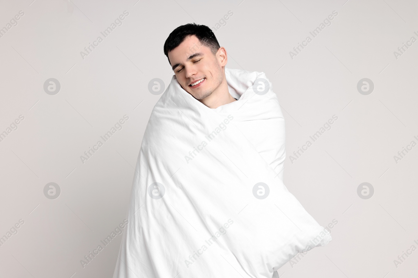 Photo of Happy man in pyjama wrapped in blanket on light grey background