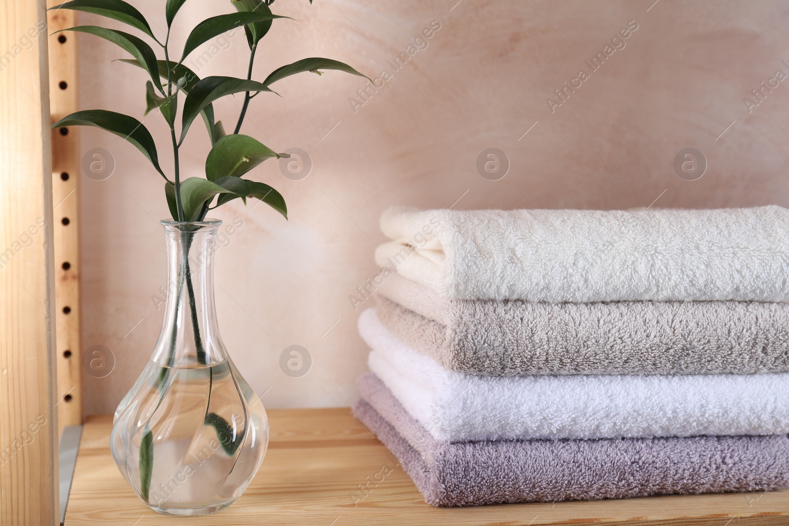 Photo of Stacked soft towels and green leaves on wooden shelf indoors