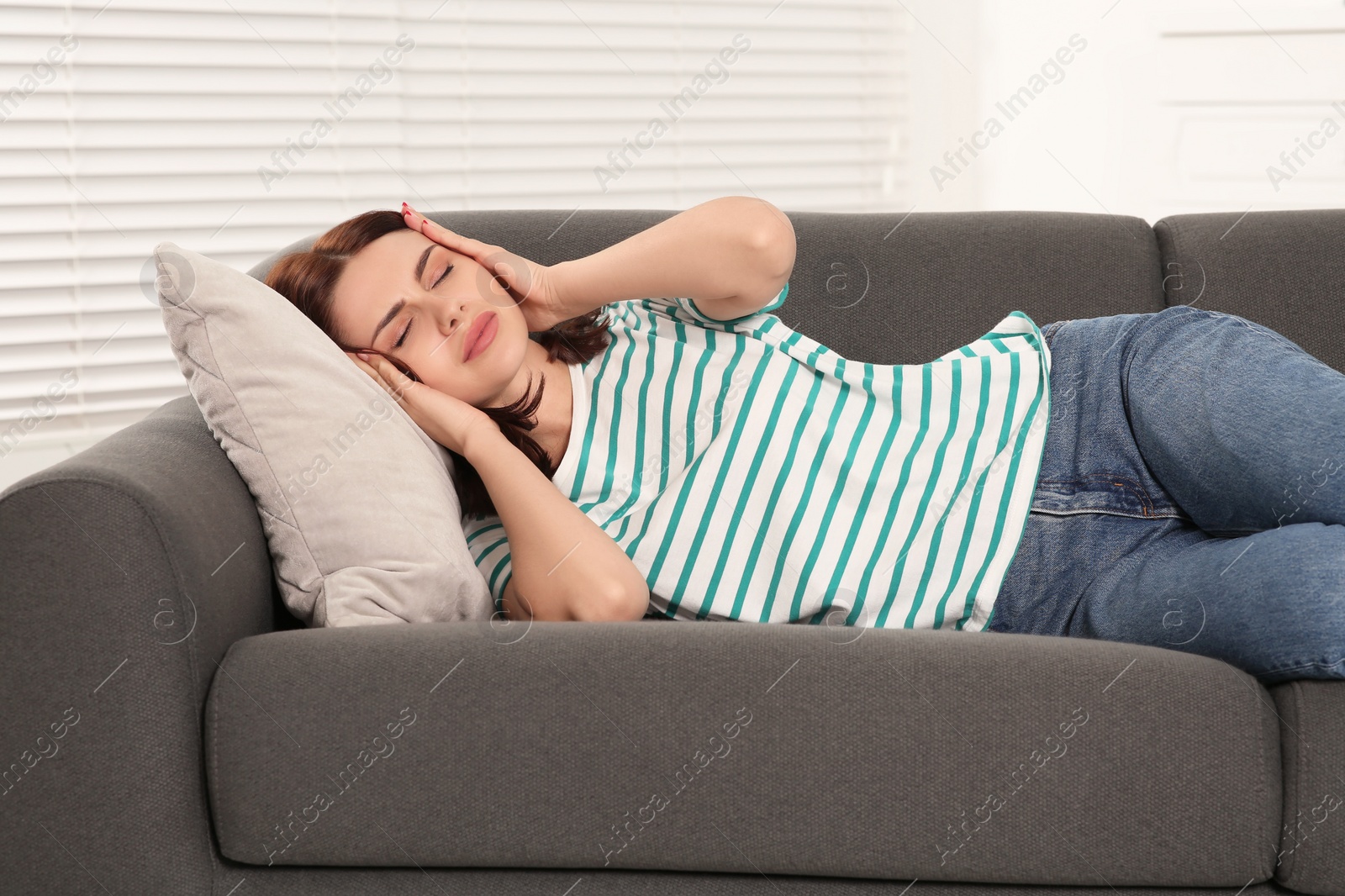 Photo of Young woman suffering from headache on sofa indoors. Hormonal disorders