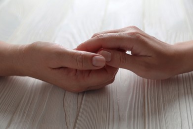 Photo of Woman holding hands with her mother at white wooden table, closeup