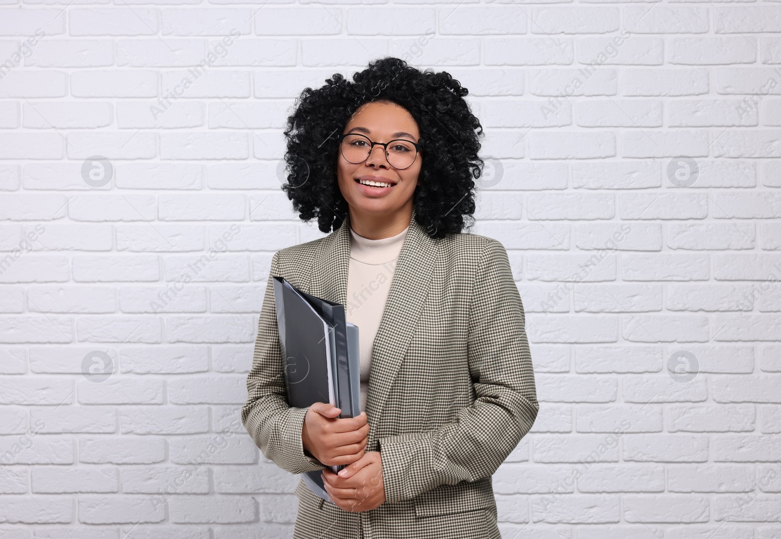 Photo of Young businesswoman with folders near white brick wall