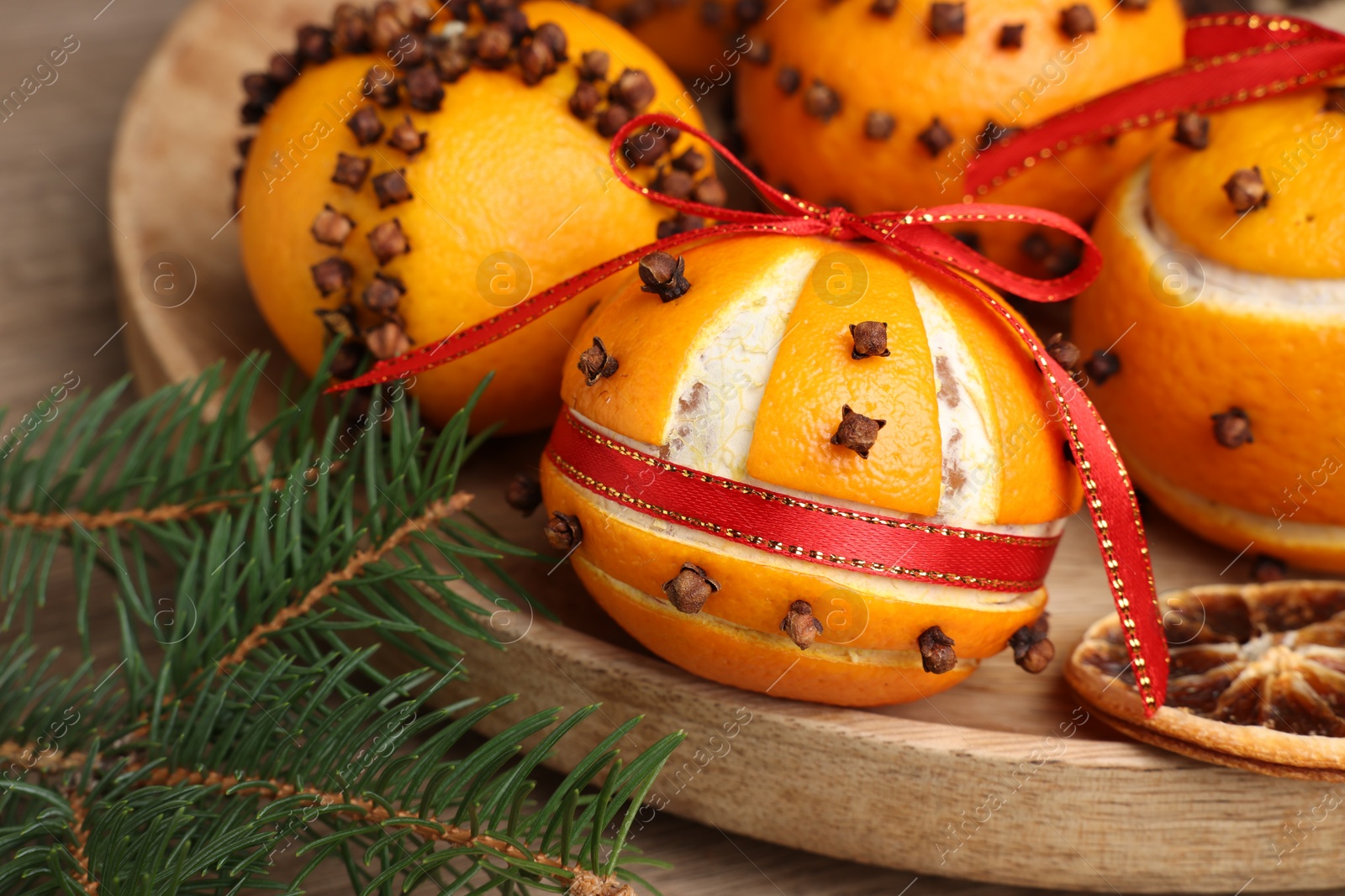 Photo of Pomander balls made of tangerines with cloves and fir branches on wooden table, closeup