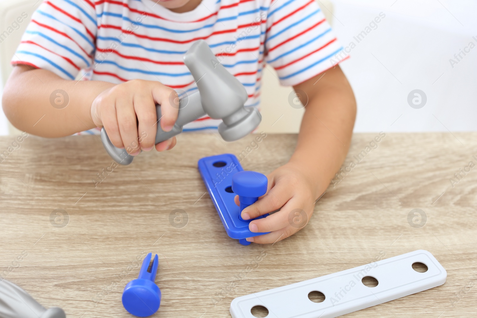 Photo of Little boy playing with toy construction tools at wooden table, closeup