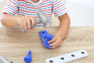 Little boy playing with toy construction tools at wooden table, closeup