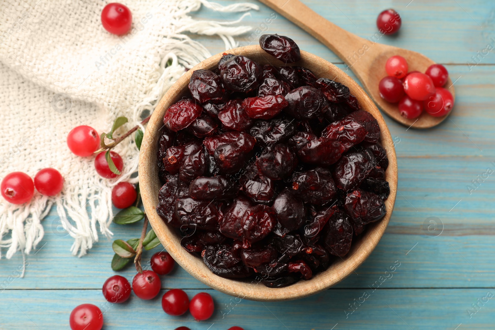 Photo of Tasty dried cranberries in bowl and fresh ones on light blue wooden table, top view