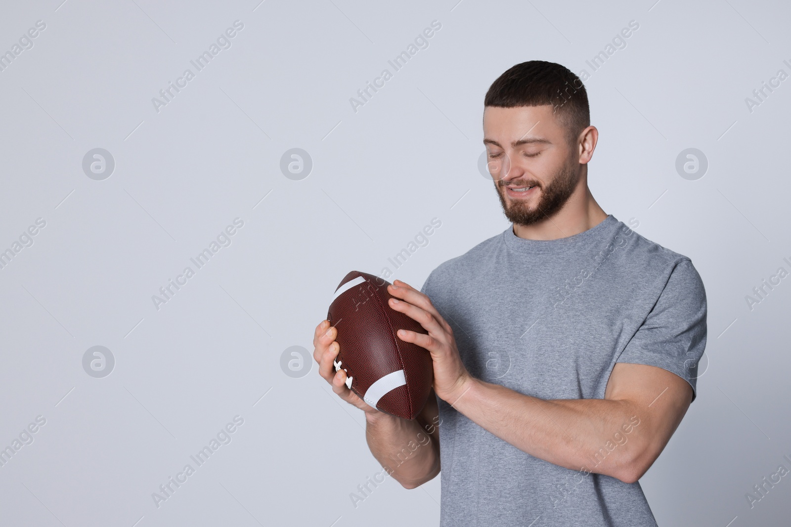 Photo of Athletic young man with American football ball on light grey background. Space for text