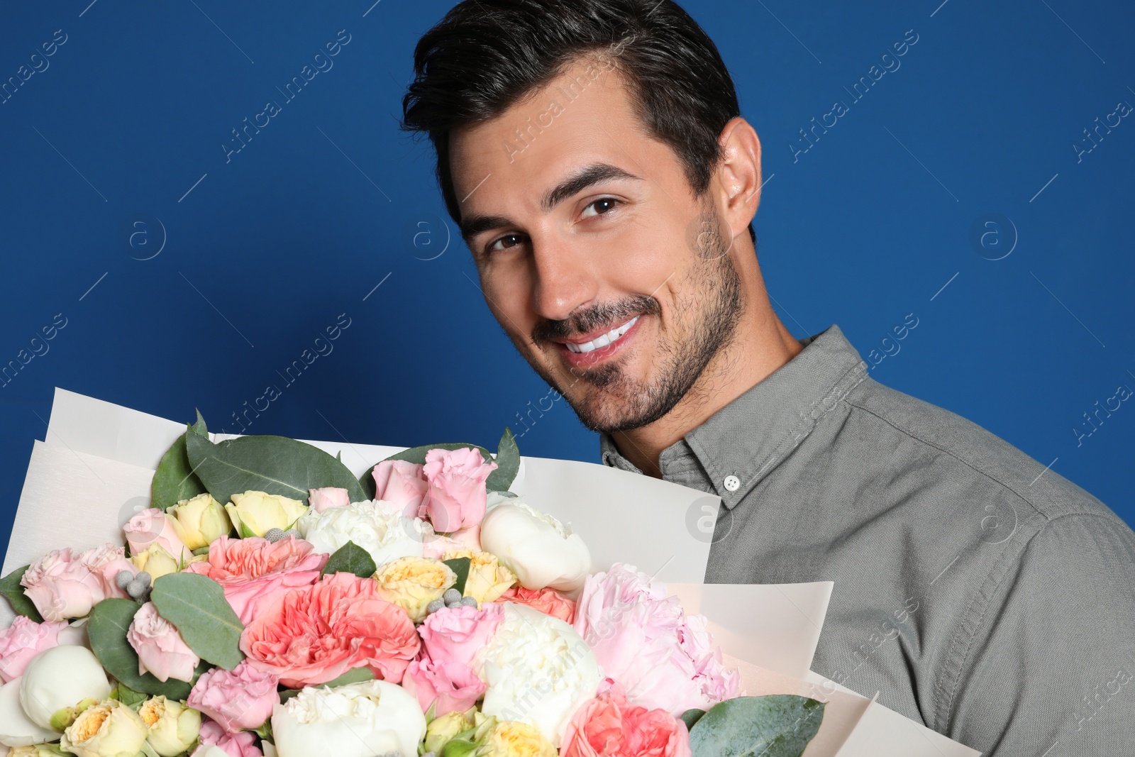 Photo of Young handsome man with beautiful flower bouquet on blue background