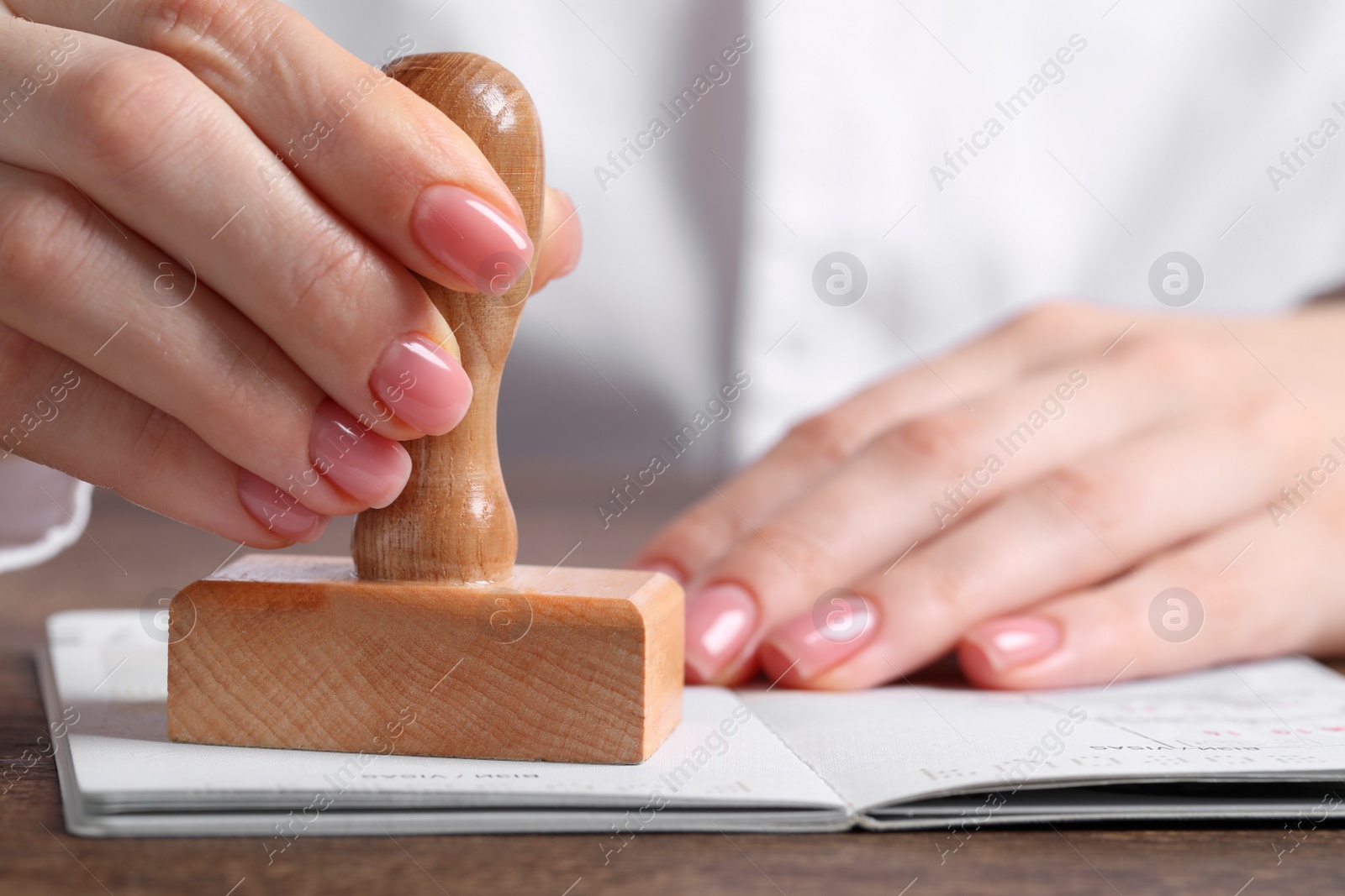 Photo of Ukraine, Lviv - September 6, 2022: Woman stamping visa page in passport at wooden table, closeup