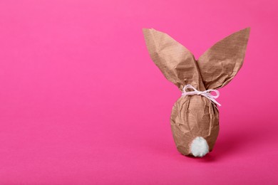 Photo of Easter bunny made of kraft paper and egg on pink background. Space for text