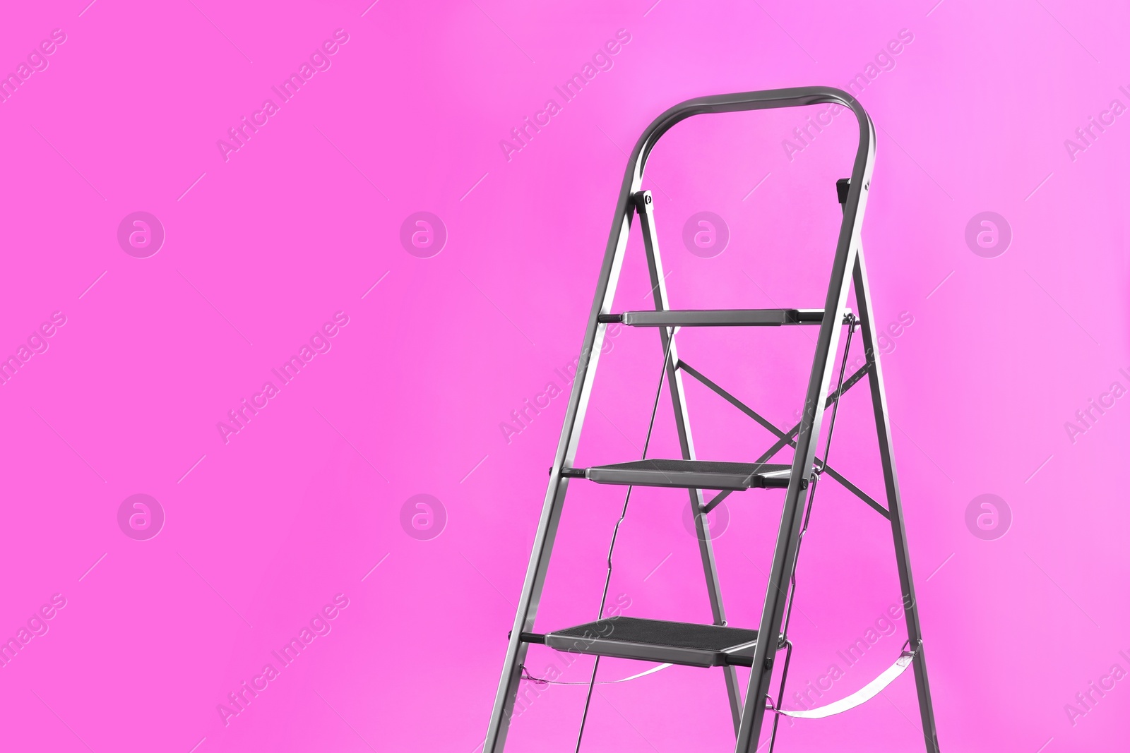 Photo of Modern metal stepladder on pink background. Space for text