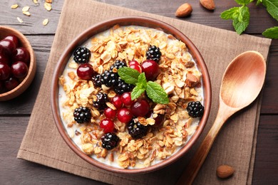 Photo of Bowl of muesli served with berries and milk on wooden table, flat lay