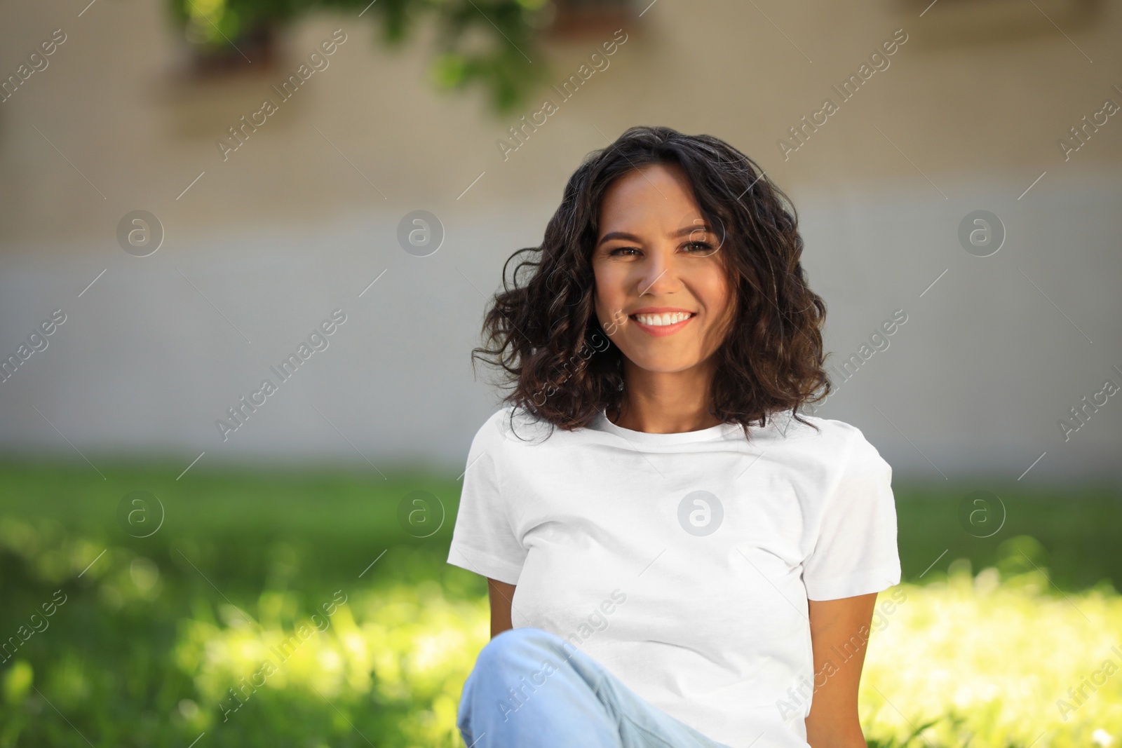 Photo of Happy young woman sitting on green grass in park on sunny day