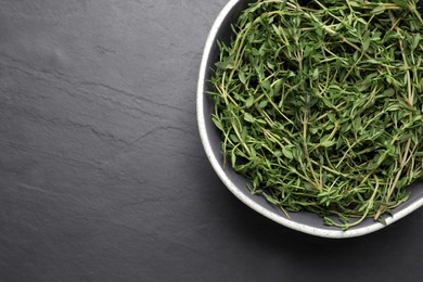 Aromatic thyme in bowl on black table, top view. Space for text