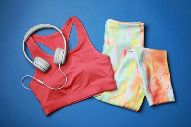 Photo of Stylish sportswear and headphones on blue background, flat lay