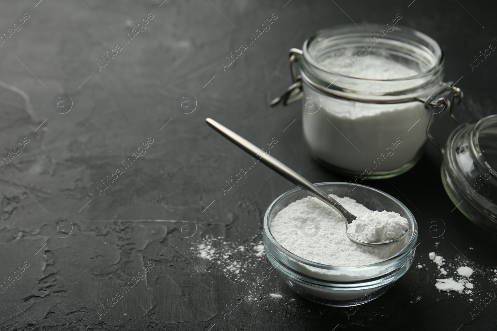 Photo of Baking powder in bowl, jar and spoon on black textured table, closeup. Space for text