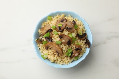 Photo of Delicious bulgur with mushrooms and green onion in bowl on white marble table, top view