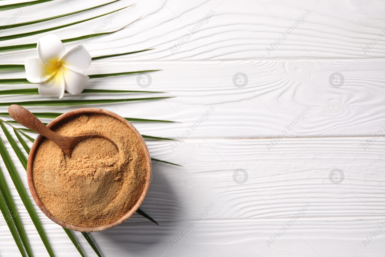 Photo of Coconut sugar and spoon in bowl on white wooden table, flat lay. Space for text