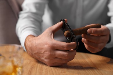 Photo of Man cutting tip of cigar at wooden table, closeup