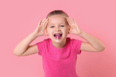 Photo of Emotional little girl eating lollipop on pink background