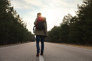 Photo of Man with backpack going along road near forest, back view