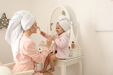 Photo of Young mother and little daughter doing makeup at dressing table