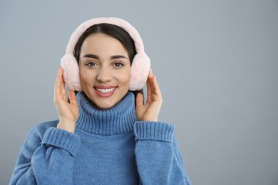 Photo of Beautiful young woman wearing earmuffs on light grey background. Space for text