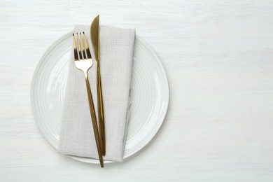 Photo of Stylish ceramic plate, cutlery and napkin on white wooden table, top view. Space for text