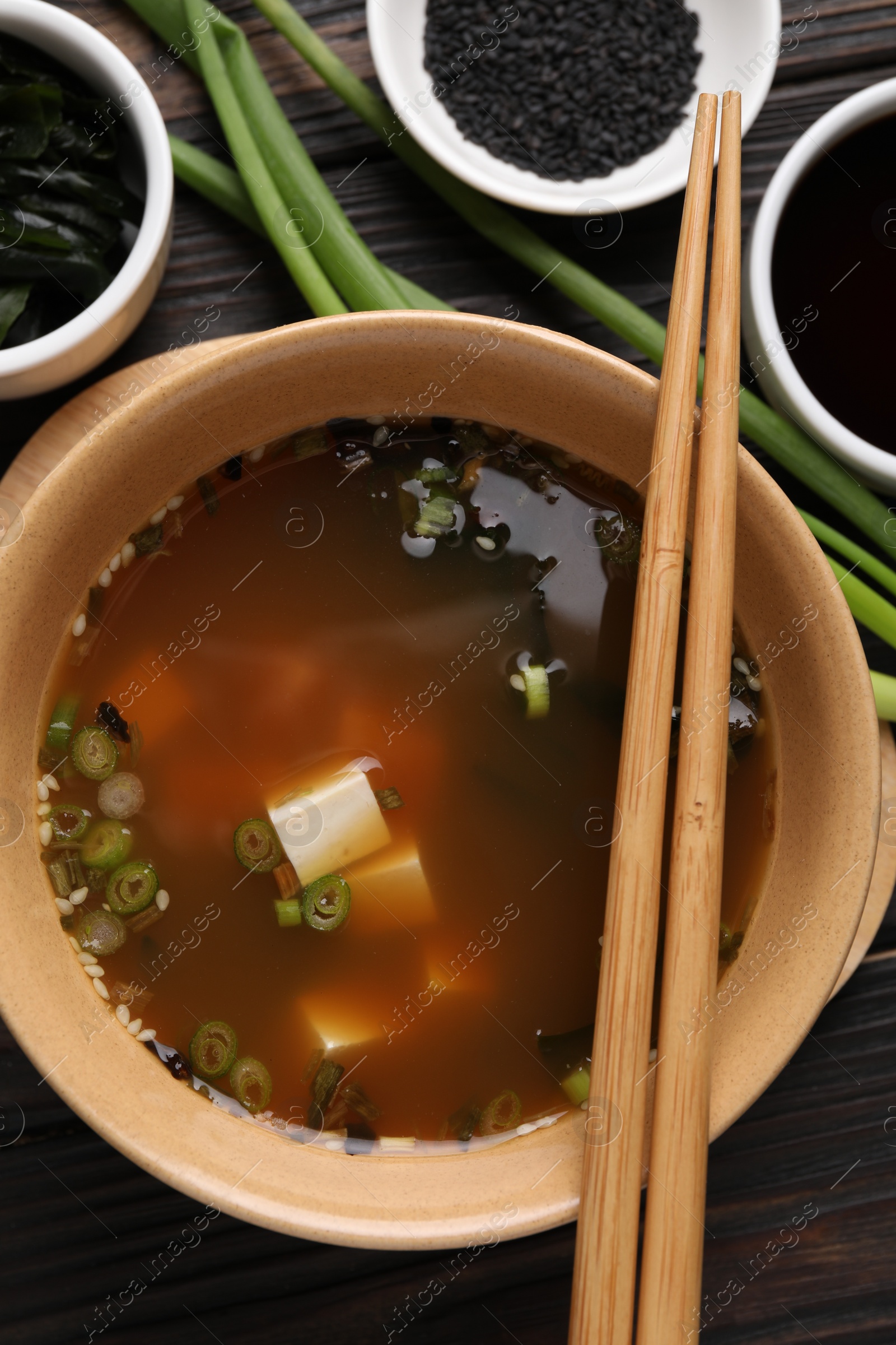 Photo of Bowl of delicious miso soup with tofu served on dark wooden table, flat lay