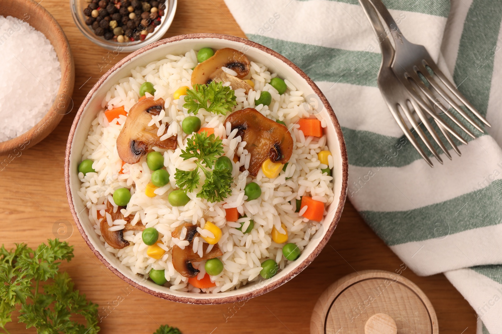 Photo of Bowl of delicious rice with vegetables on wooden table, flat lay