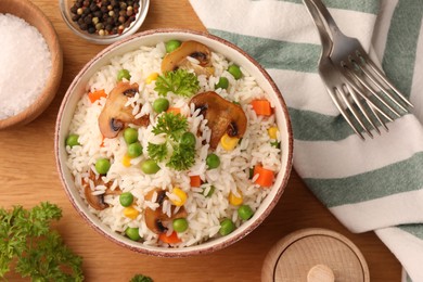 Bowl of delicious rice with vegetables on wooden table, flat lay