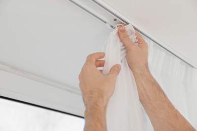 Photo of Worker hanging window curtain indoors, closeup view
