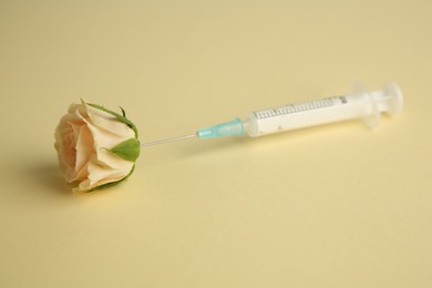 Photo of Medical syringe and beautiful rose on pale yellow background, closeup