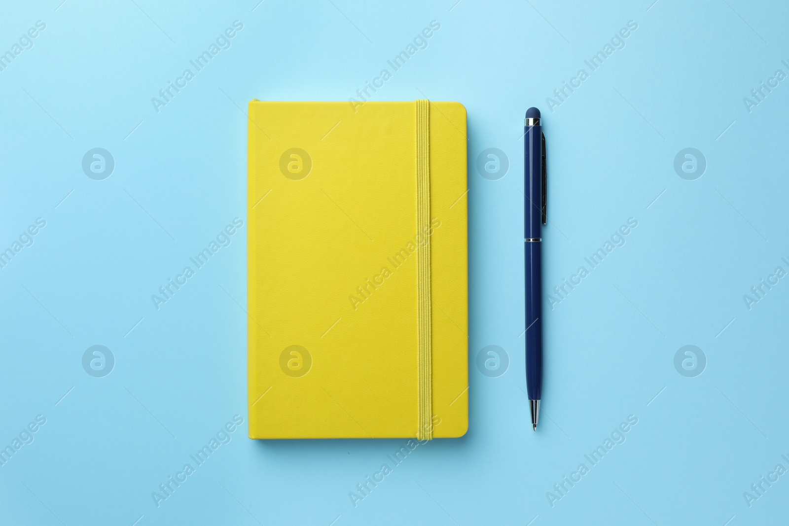 Photo of Closed yellow notebook and pen on light blue background, top view