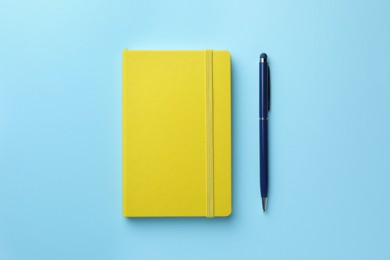 Closed yellow notebook and pen on light blue background, top view