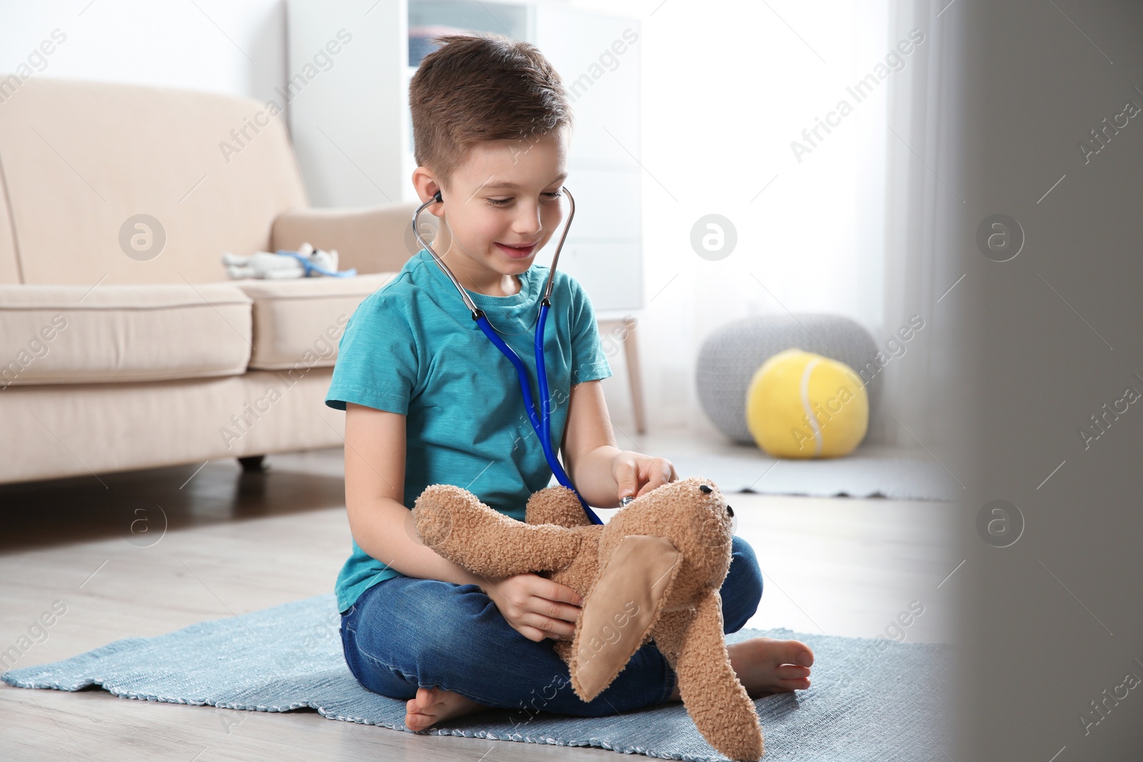 Photo of Cute child imagining himself as doctor while playing with stethoscope and toy bunny at home