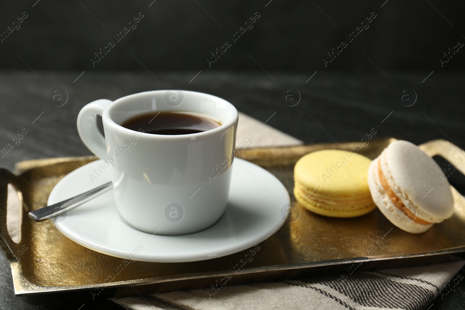 Photo of Tray with hot coffee in cup and macarons on dark textured table, closeup