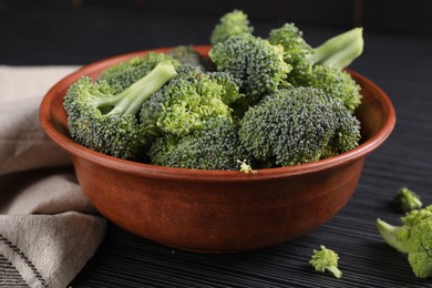 Photo of Bowl with fresh raw broccoli on black wooden table, closeup