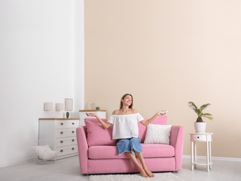 Happy young woman sitting under air conditioner at home