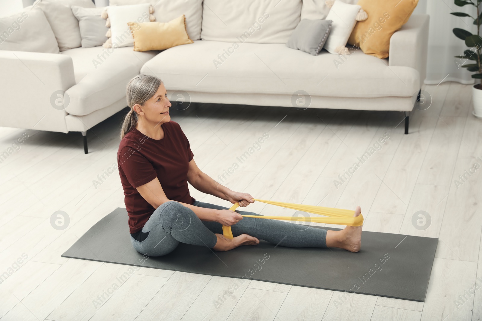 Photo of Senior woman doing exercise with fitness elastic band on mat at home