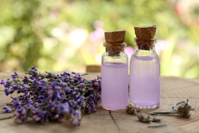 Beautiful lavender flowers and bottles of essential oil on wooden stump, closeup