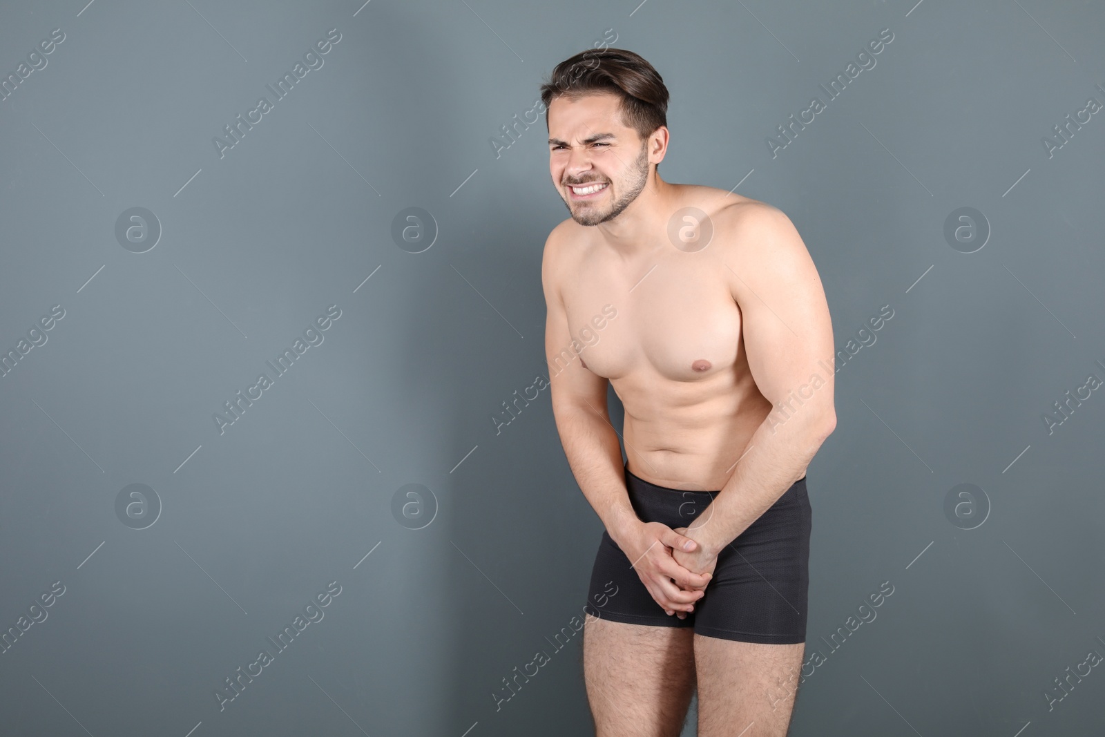 Photo of Young man with urological problems suffering from pain on grey background