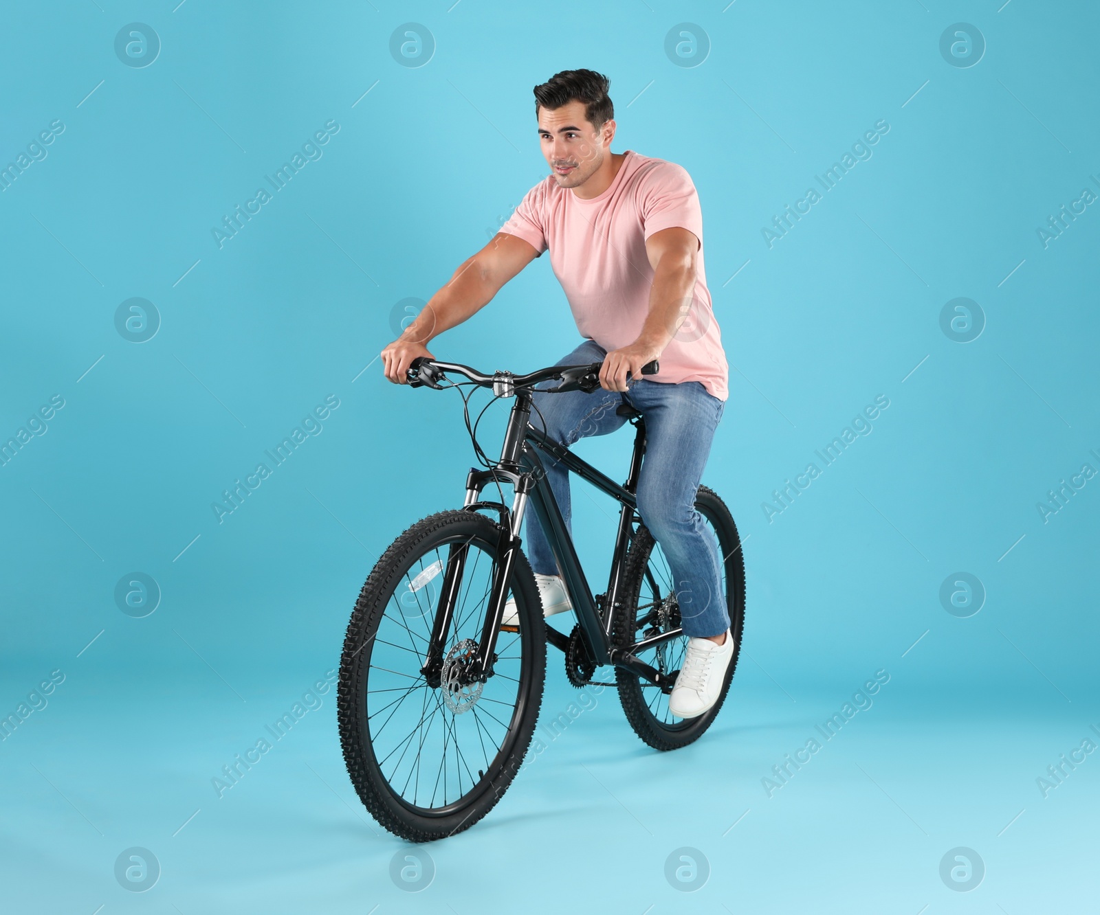 Photo of Handsome young man with modern bicycle on light blue background