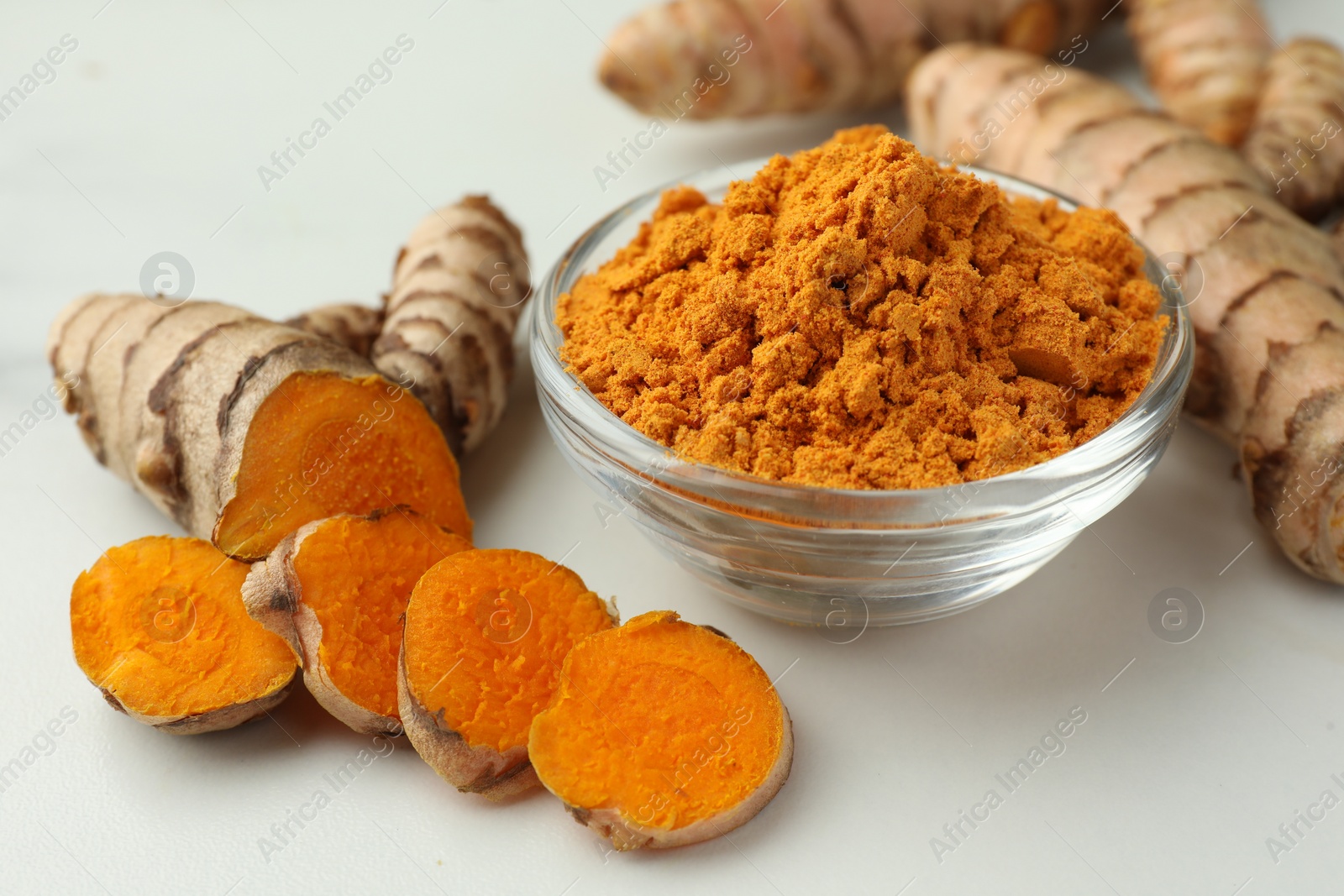 Photo of Aromatic turmeric powder and raw roots on white table, closeup