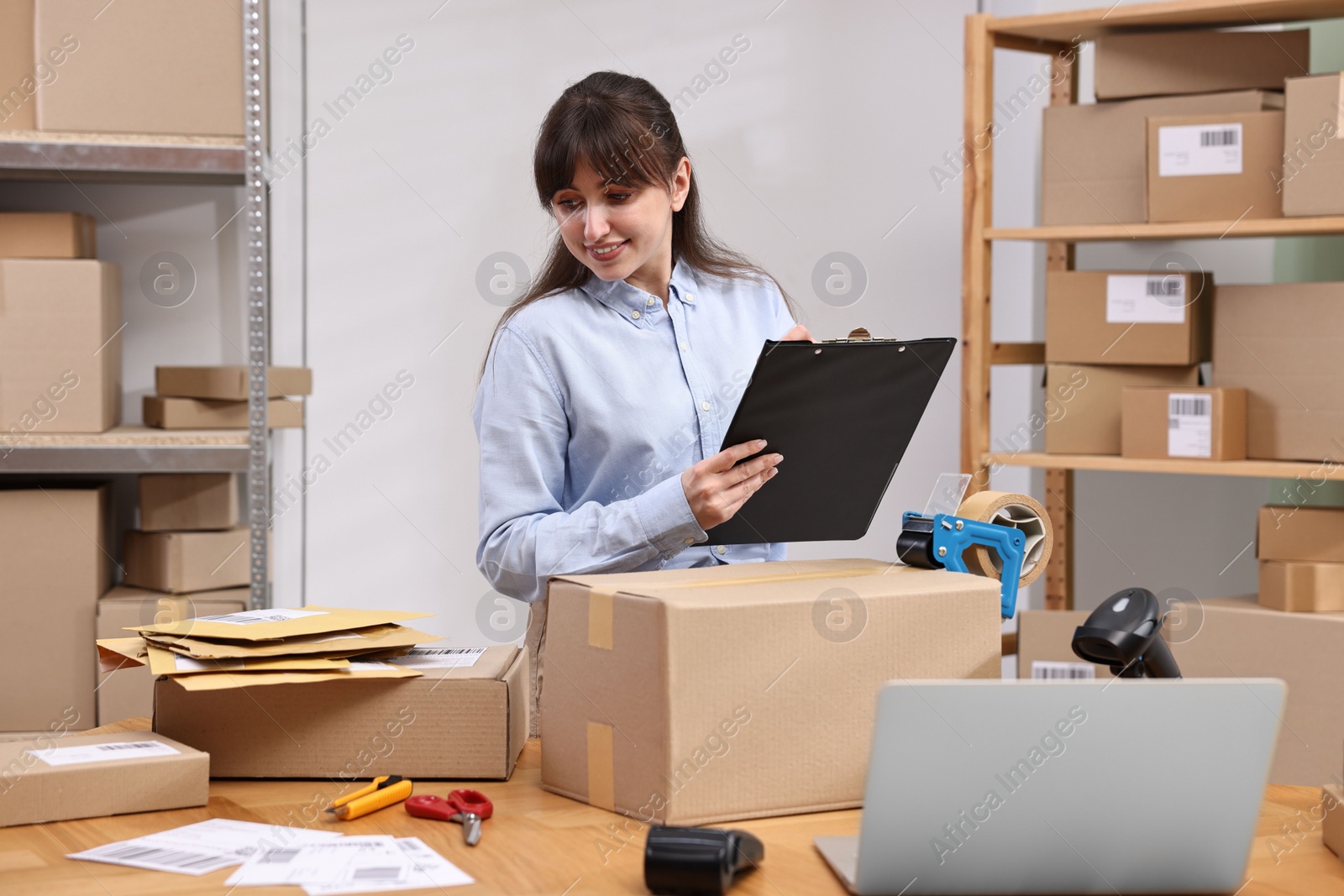 Photo of Parcel packing. Post office worker with clipboard writing notes at wooden table indoors