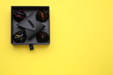 Photo of Box of tasty chocolate candies on yellow background, top view. Space for text