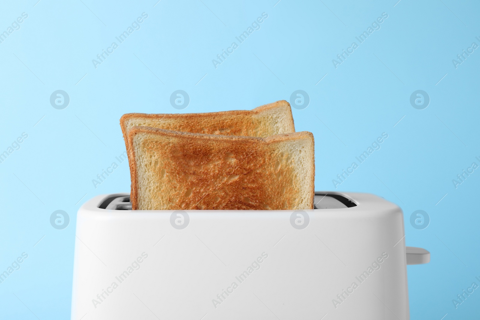 Photo of Modern toaster with slices of bread on light blue background, closeup