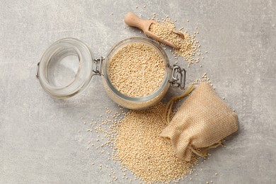 Dry quinoa seeds in glass jar and sack on light grey table, flat lay