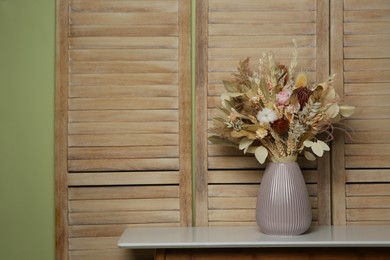 Beautiful dried flower bouquet in ceramic vase on white table near wooden folding screen. space for text